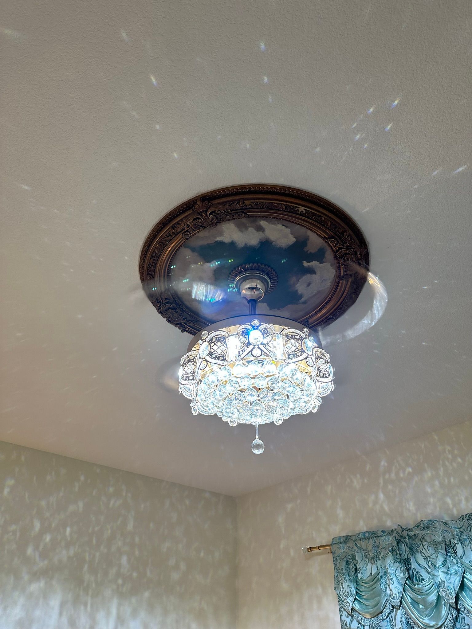 Ornate ceiling light with crystal accents, casting light onto a white ceiling and wall.