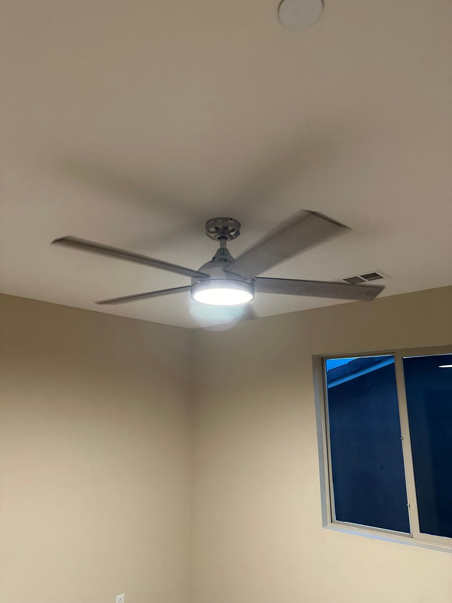 Ceiling fan with light fixture in a room with beige walls and a window.