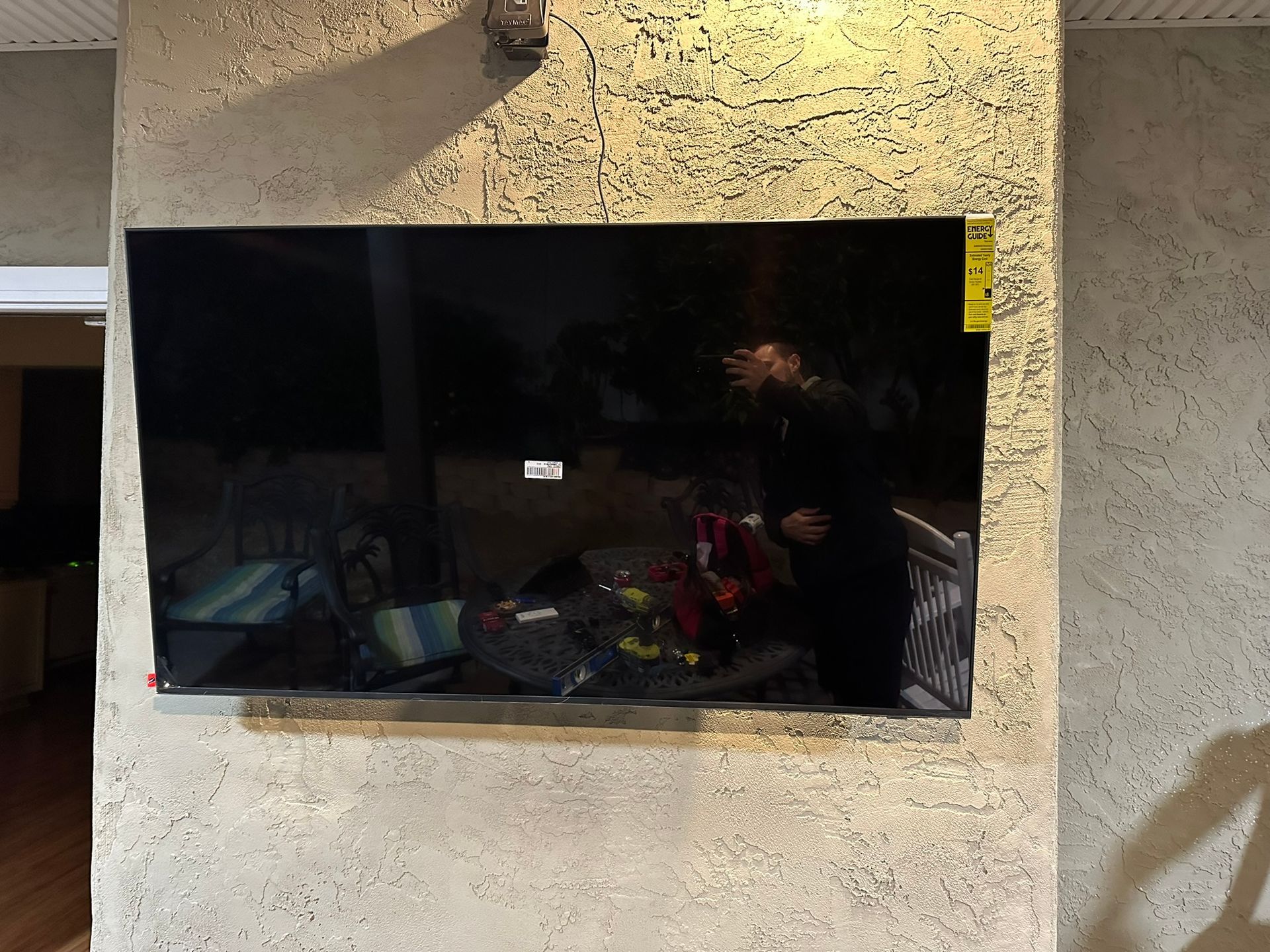Flat screen TV mounted on a textured, gray wall with visible reflection.
