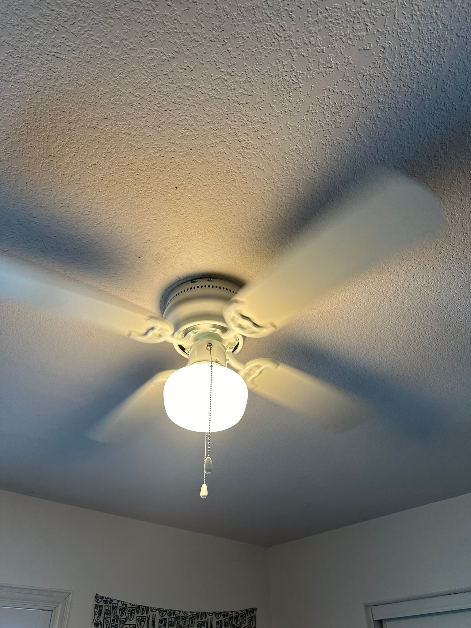 Ceiling fan with light illuminating the blades, mounted on a textured white ceiling.