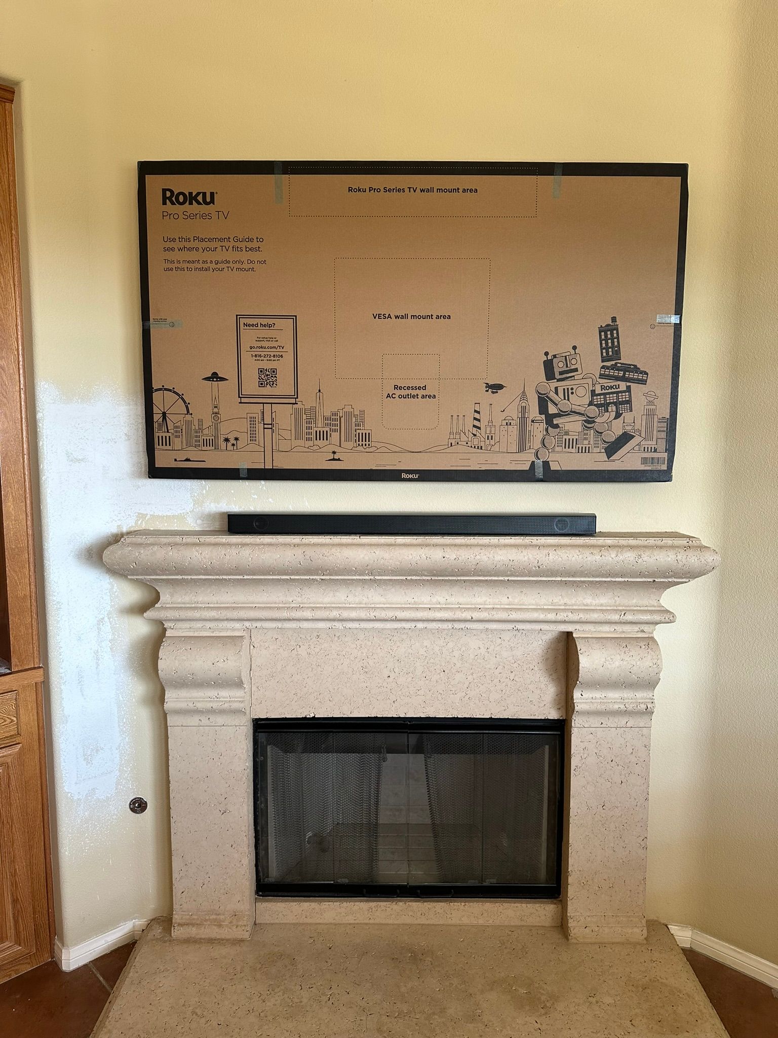A fireplace with a light-colored stone mantel. Above it hangs a large brown cardboard box.