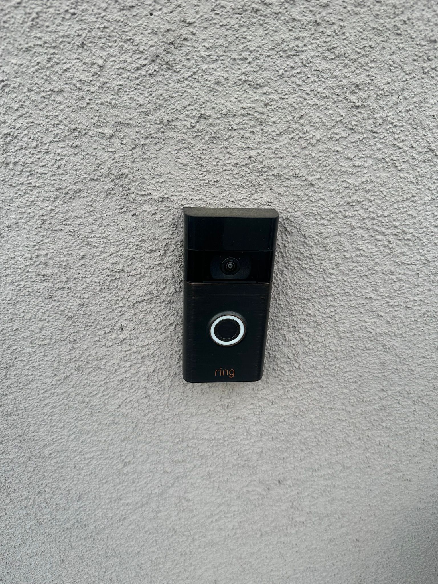 Black video doorbell mounted on a gray stucco wall