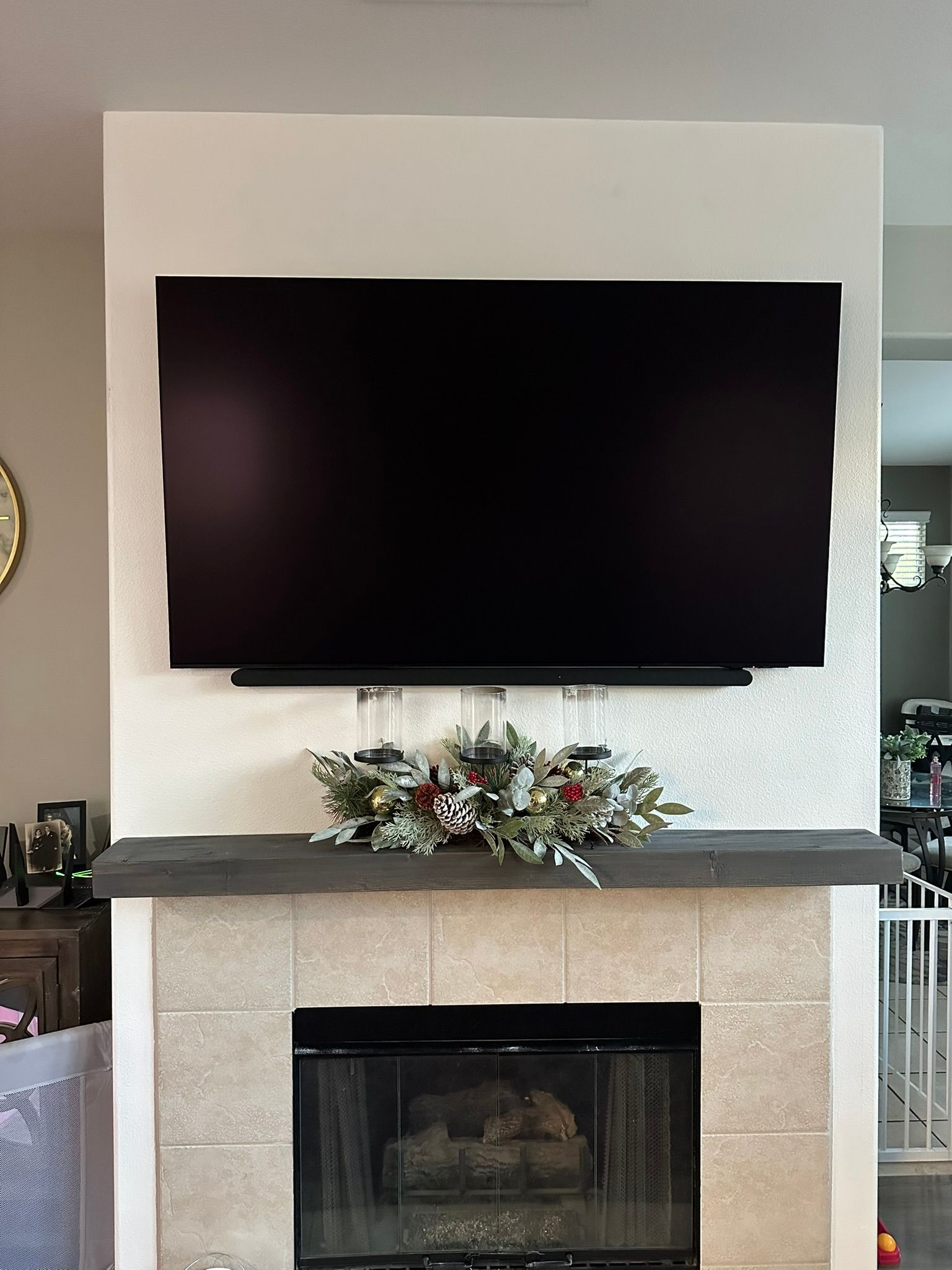 A television mounted above a fireplace, decorated with greenery and candles.