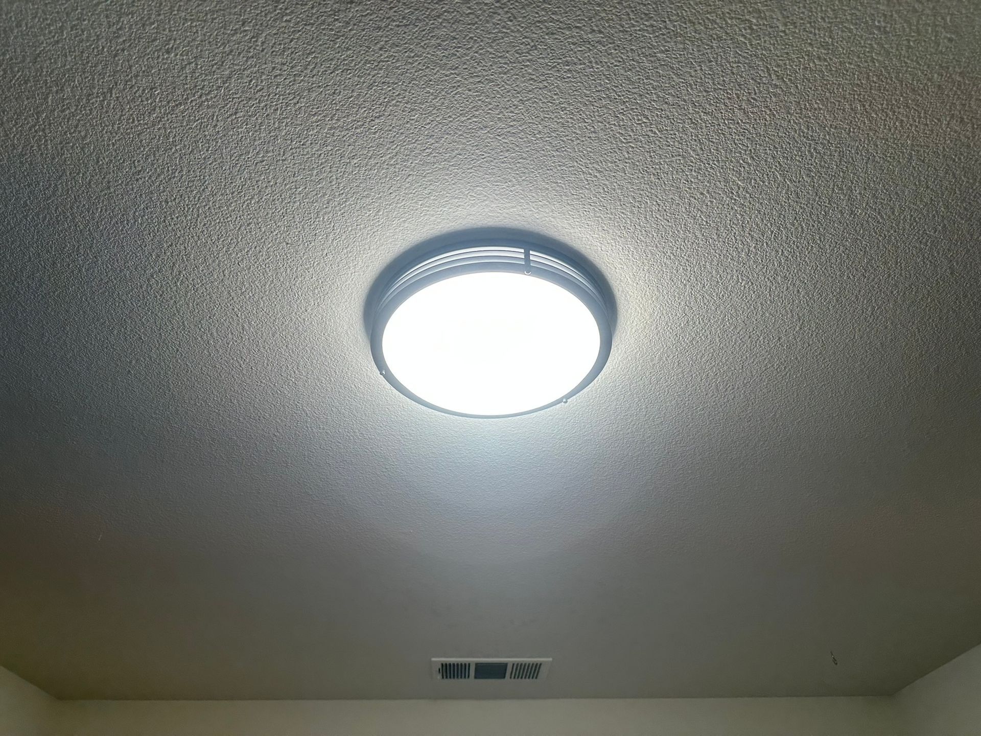 Round ceiling light fixture illuminating a textured ceiling and a small section of wall below.