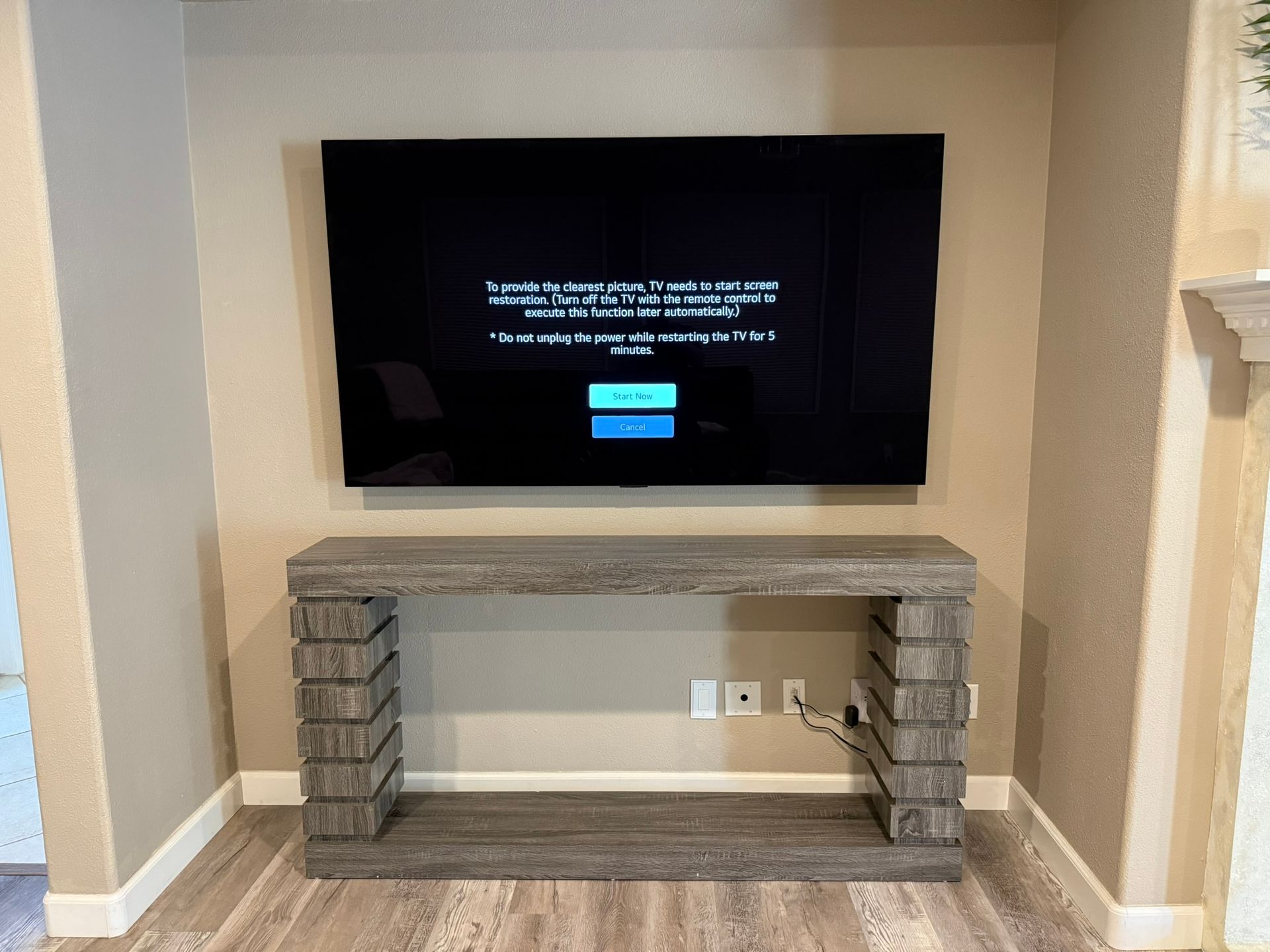 A flat-screen TV on a wall above a gray console table. The TV displays a black screen with text.