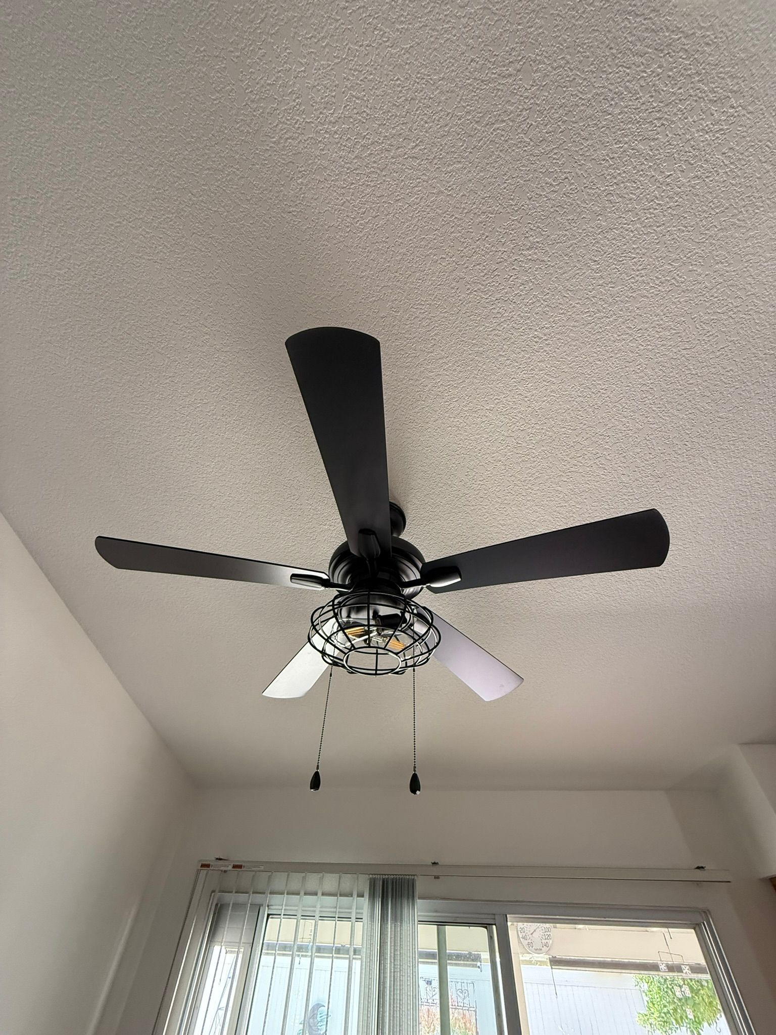 Black ceiling fan with five blades on a textured white ceiling.