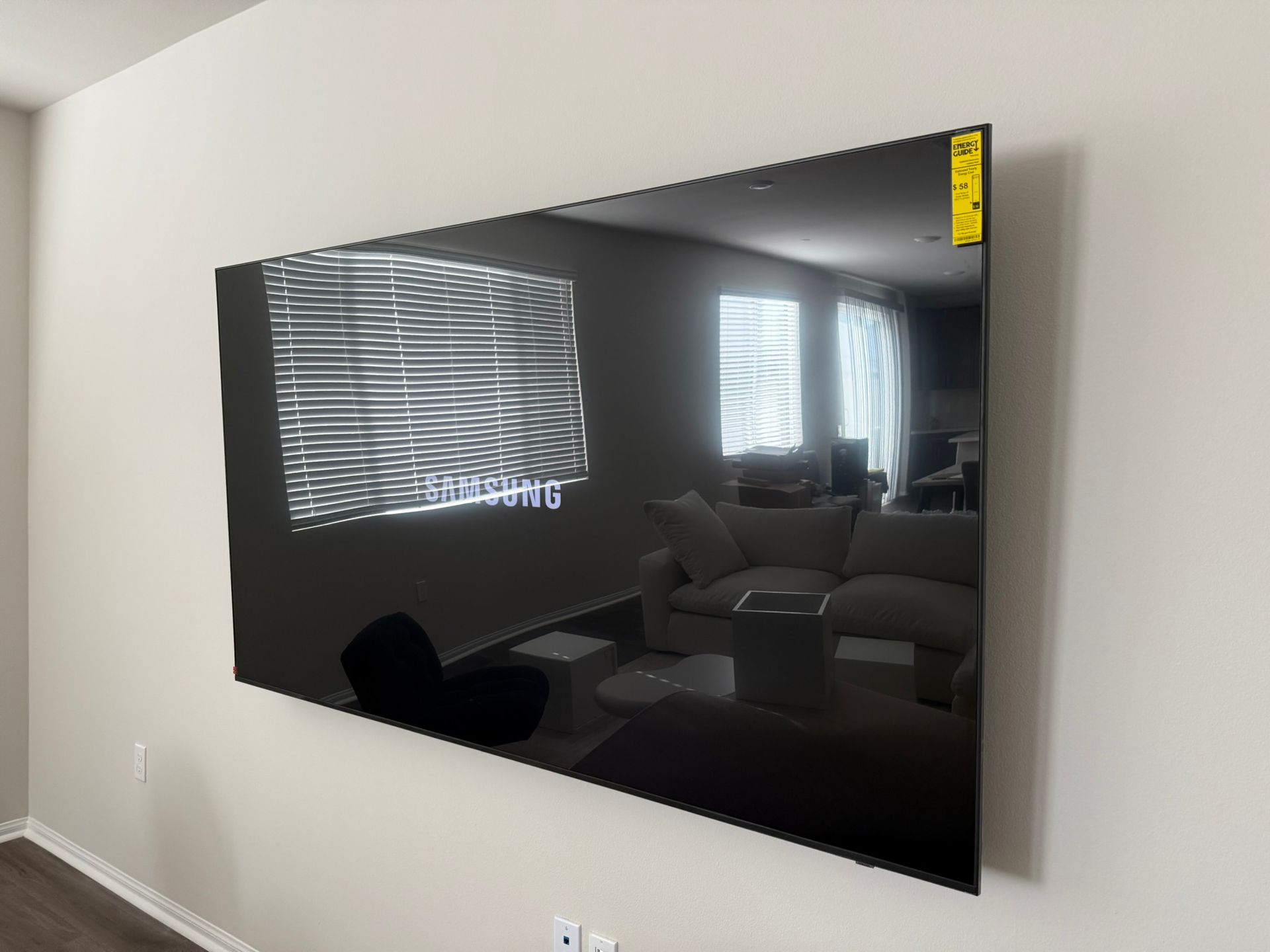 Large black TV mounted on a light wall, reflecting a living room.