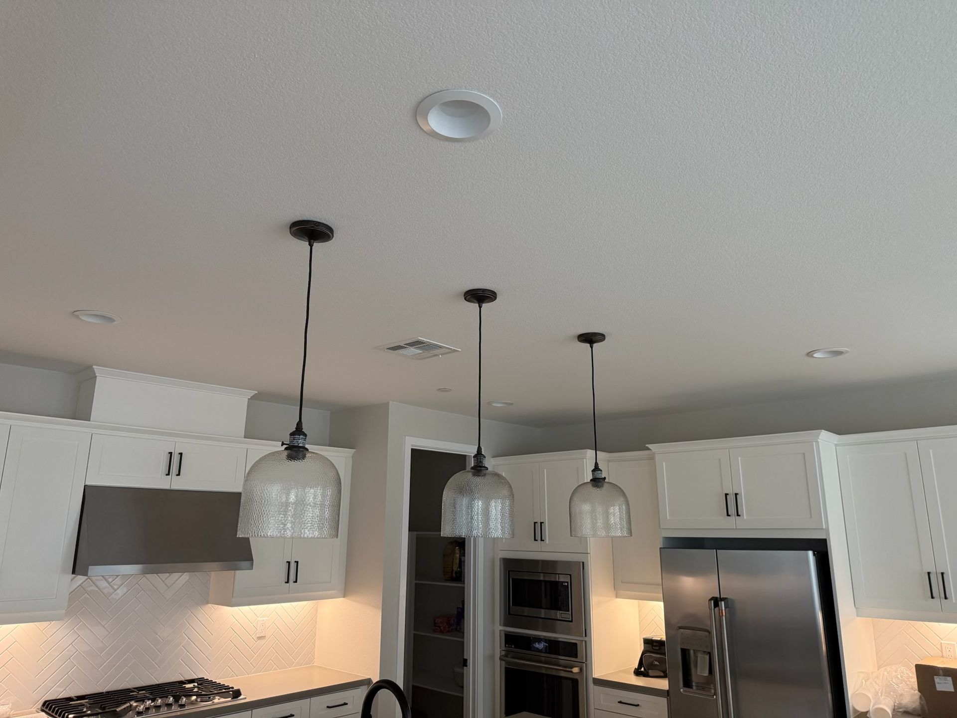 Kitchen with white cabinets, stainless steel appliances, and three pendant lights hanging from the ceiling.