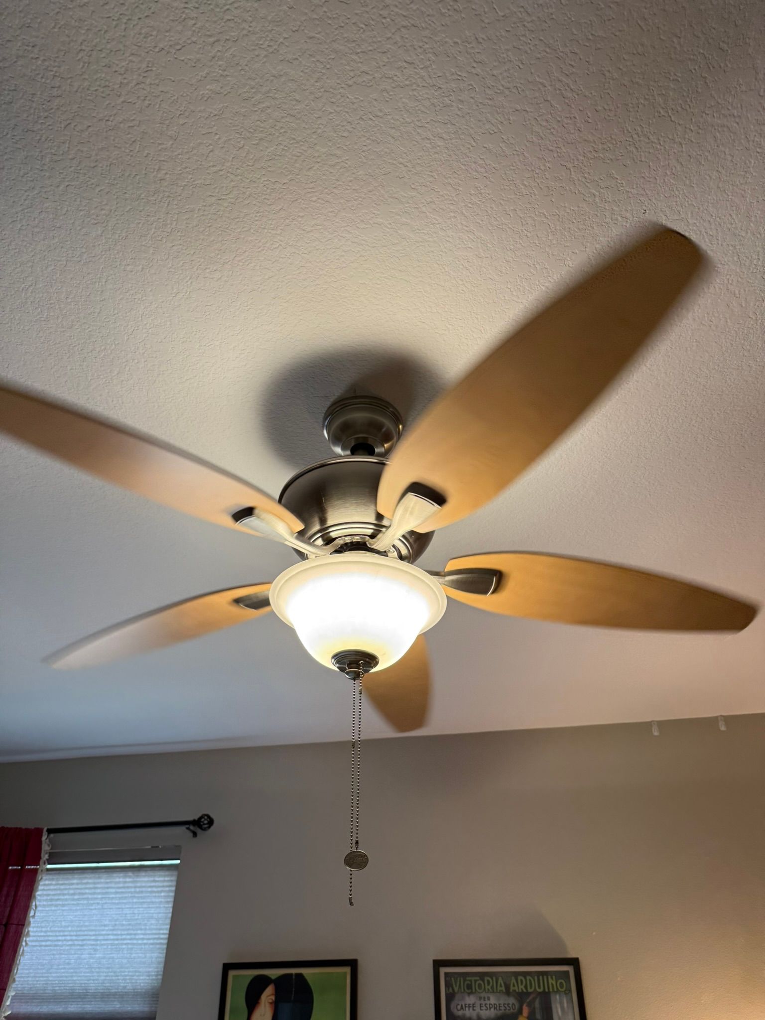 Ceiling fan with five wood blades and a light fixture, spinning against a white ceiling.