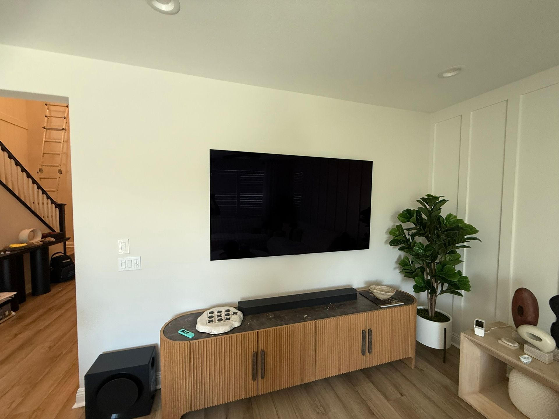 Living room with wall-mounted TV, wooden cabinet, and faux potted plant.