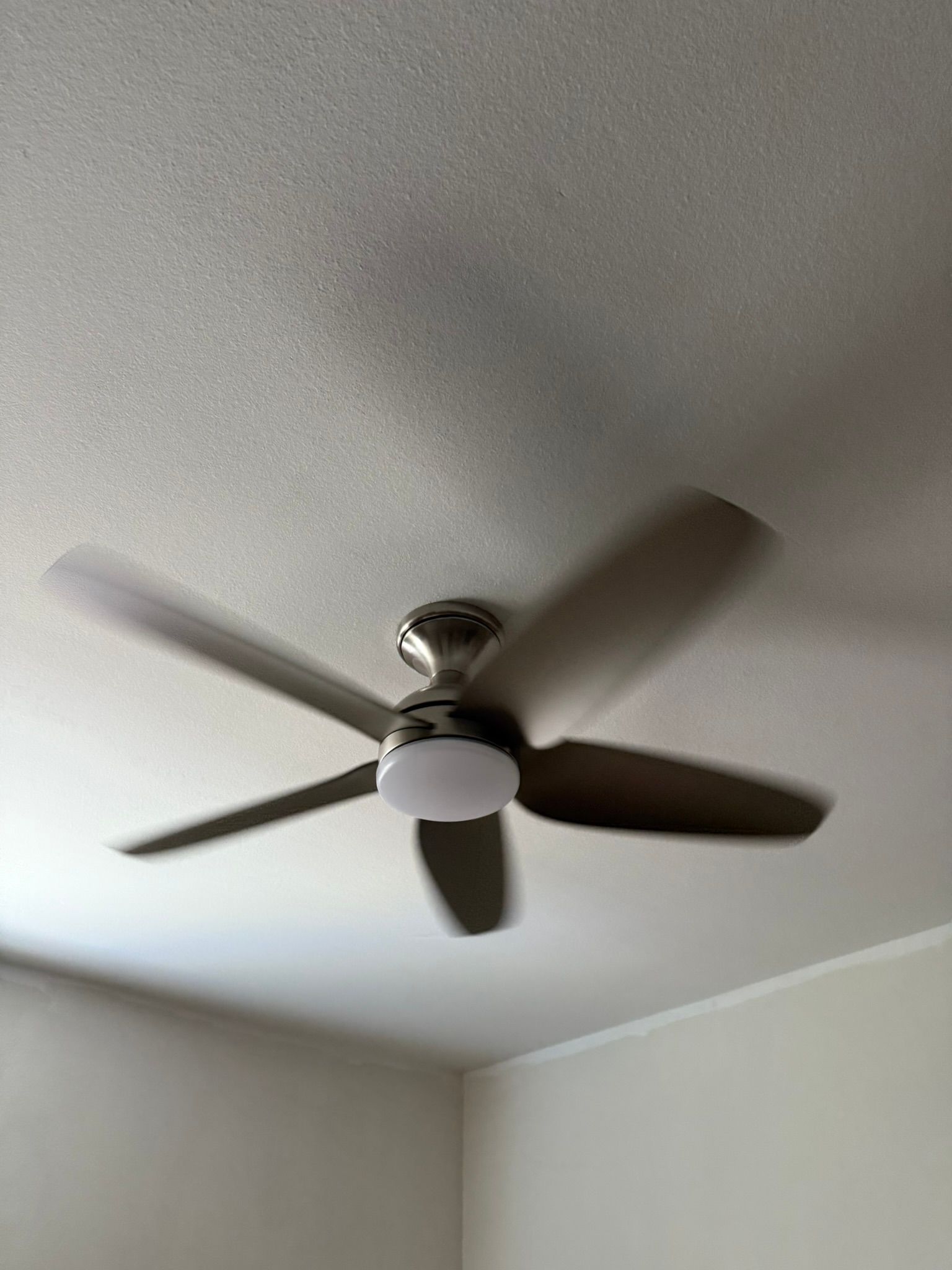 Ceiling fan with five blades, spinning, mounted on a white ceiling.