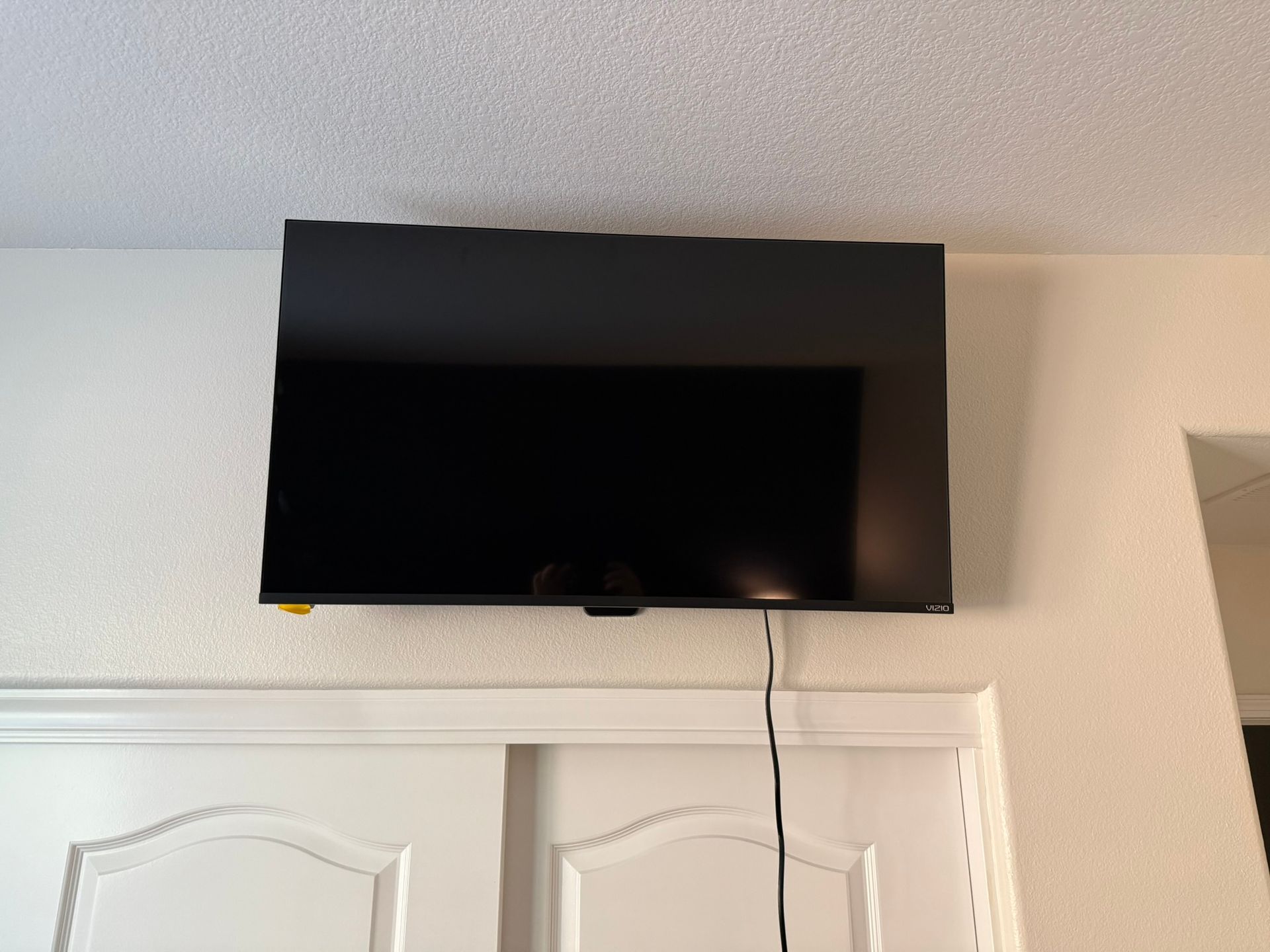 Black TV mounted on a white wall above a closed white closet door. Black cable hangs down.
