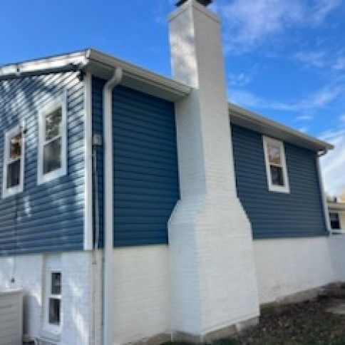 Blue-sided house with white trim and a large white chimney against a blue sky.