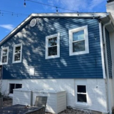 Blue-sided house with white trim and foundation, several windows, and a sunny sky.