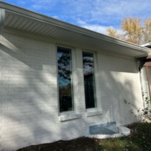 White brick house with two tall windows, a gutter, and a cloudy blue sky.