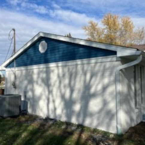 Side view of a house with white stucco walls, blue gabled roof, and white trim.
