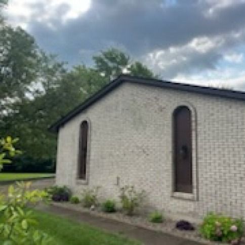 A white brick building with arched windows and a dark roof, under a cloudy sky.