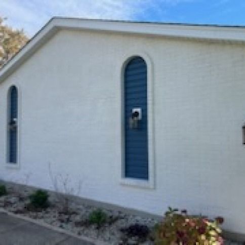White stucco building with arched blue window frames, next to greenery.