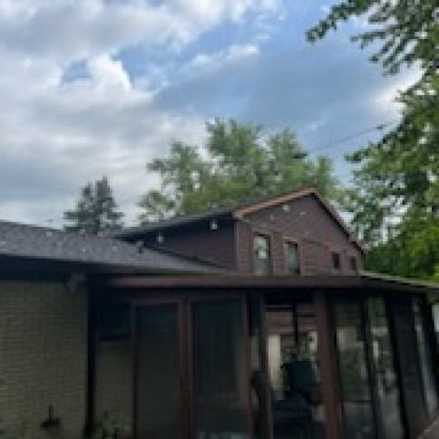 House with a dark roof and a screened porch, set against a cloudy sky.