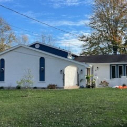 White building with blue accents and arched doorway. Green lawn under blue sky.