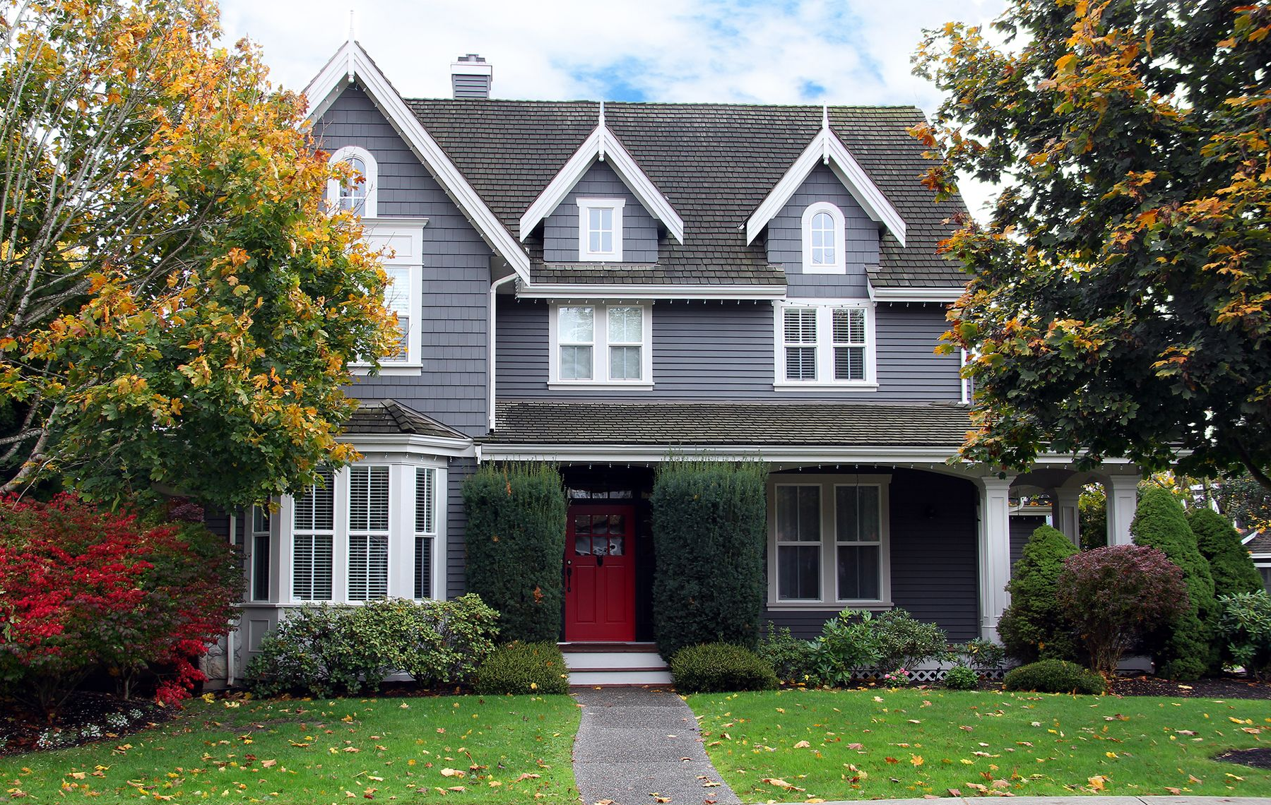 Gray house with red door, white trim, and autumn trees.