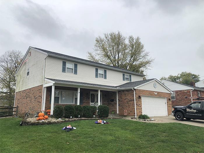 Two-story house with brick and siding, green lawn, cloudy sky.