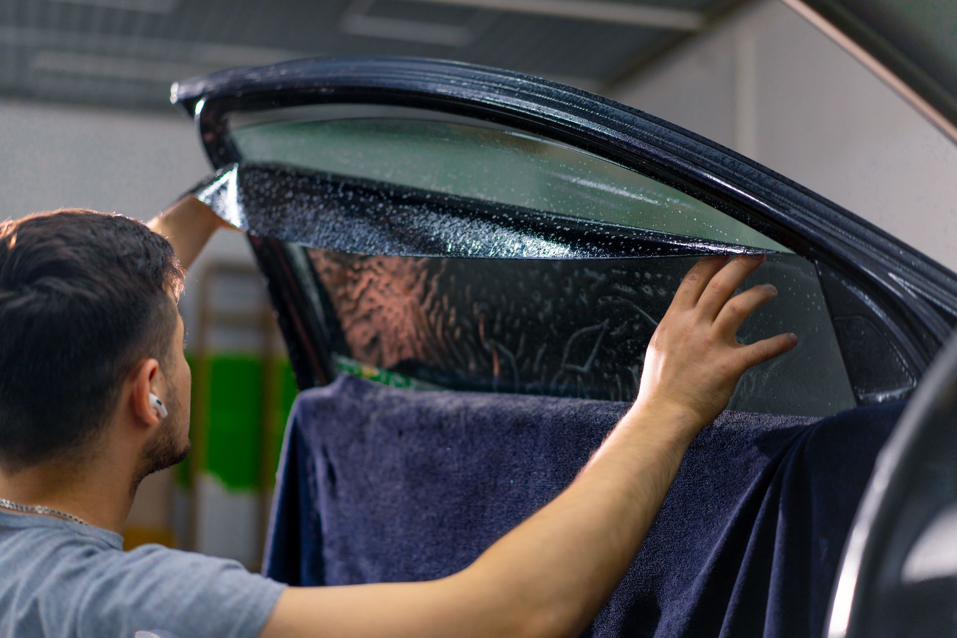 Man installing dark tint film on a car window inside a garage