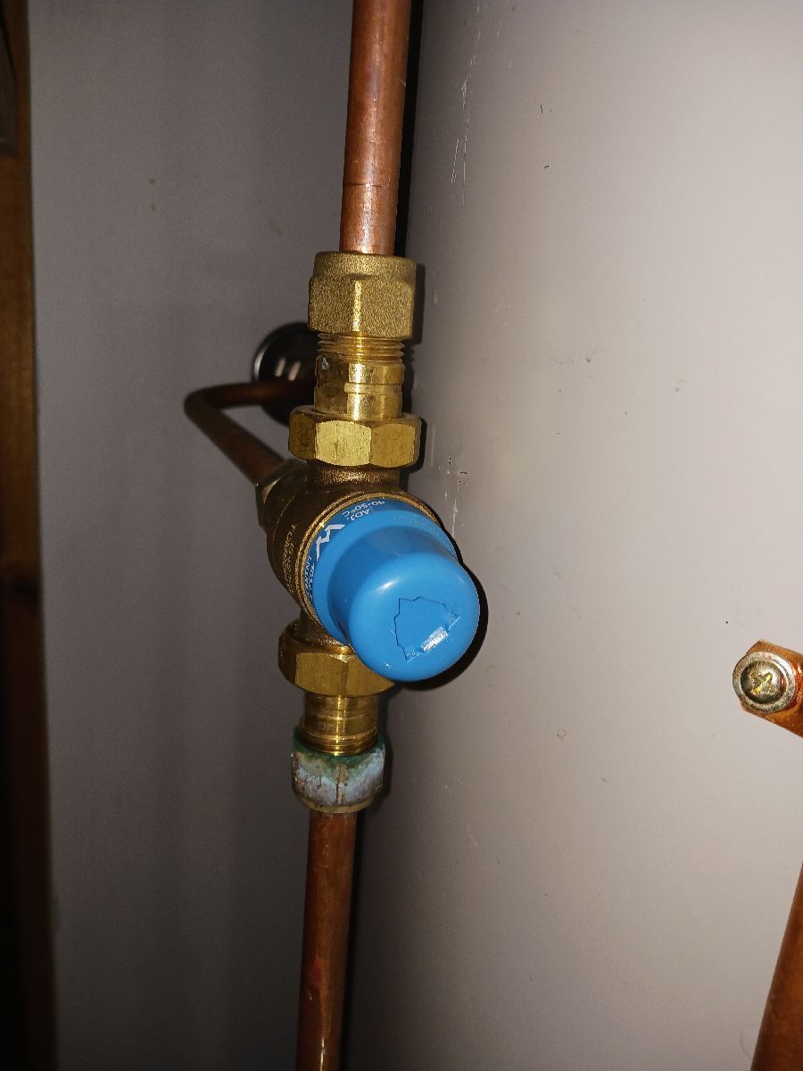 A Blue Cap Connected to Vertical Copper Pipes Against a Plain Wall — Dunnrite Plumbing Services in Cannonvale, QLD