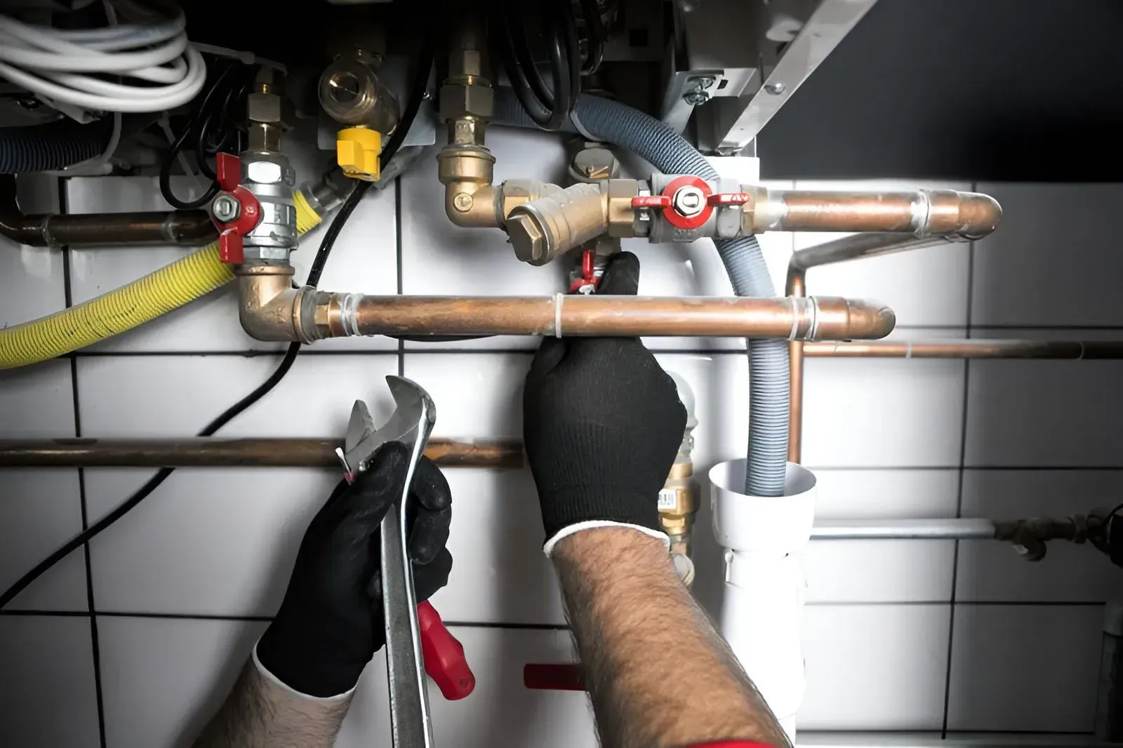 A Person Uses a Wrench to Adjust Copper Pipes — Dunnrite Plumbing Services in Airlie Beach, QLD