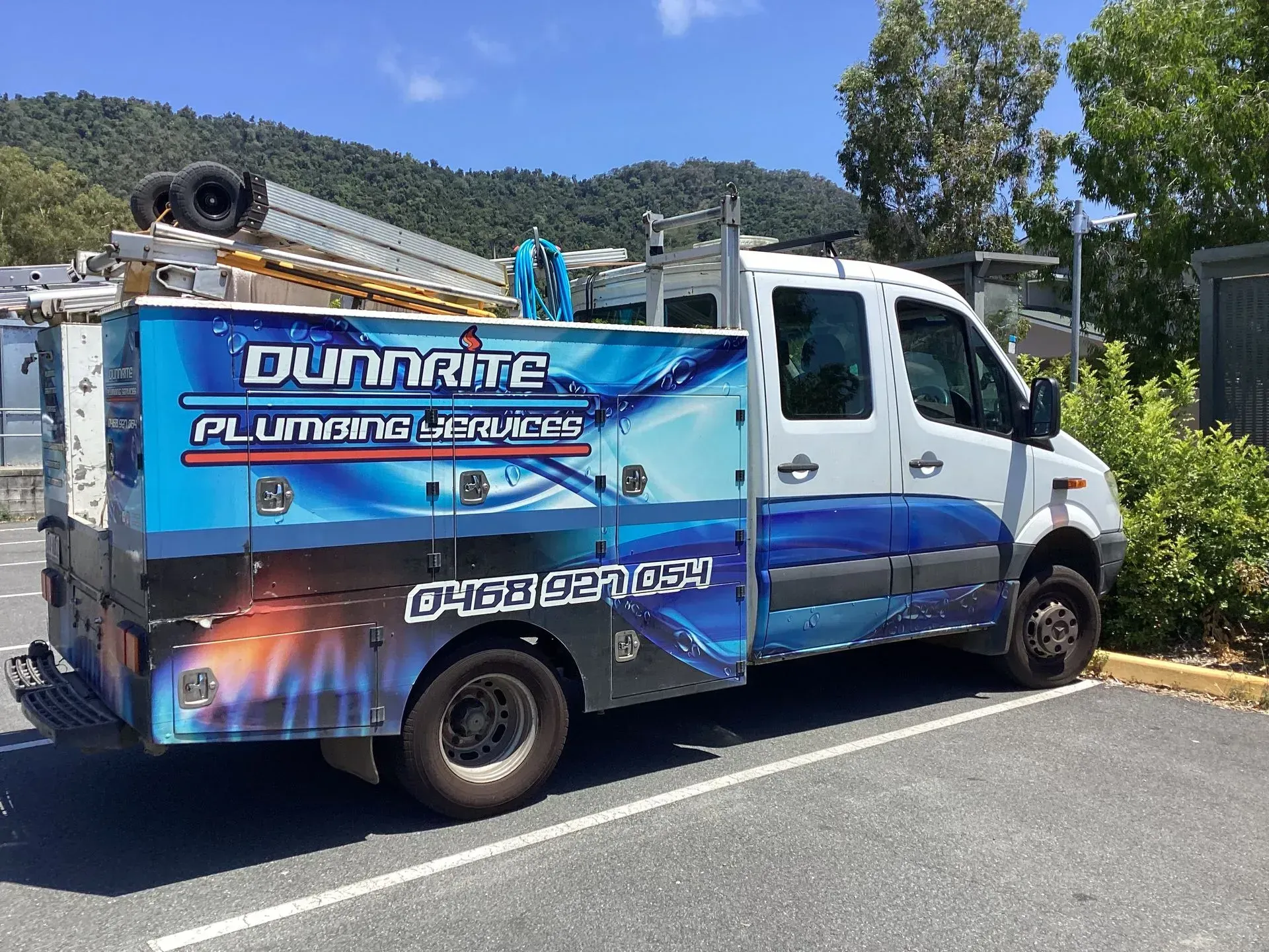 White Utility Truck Parked on a Road, Carrying Ladders and Equipment on Top — Dunnrite Plumbing Services in Cannonvale, QLD