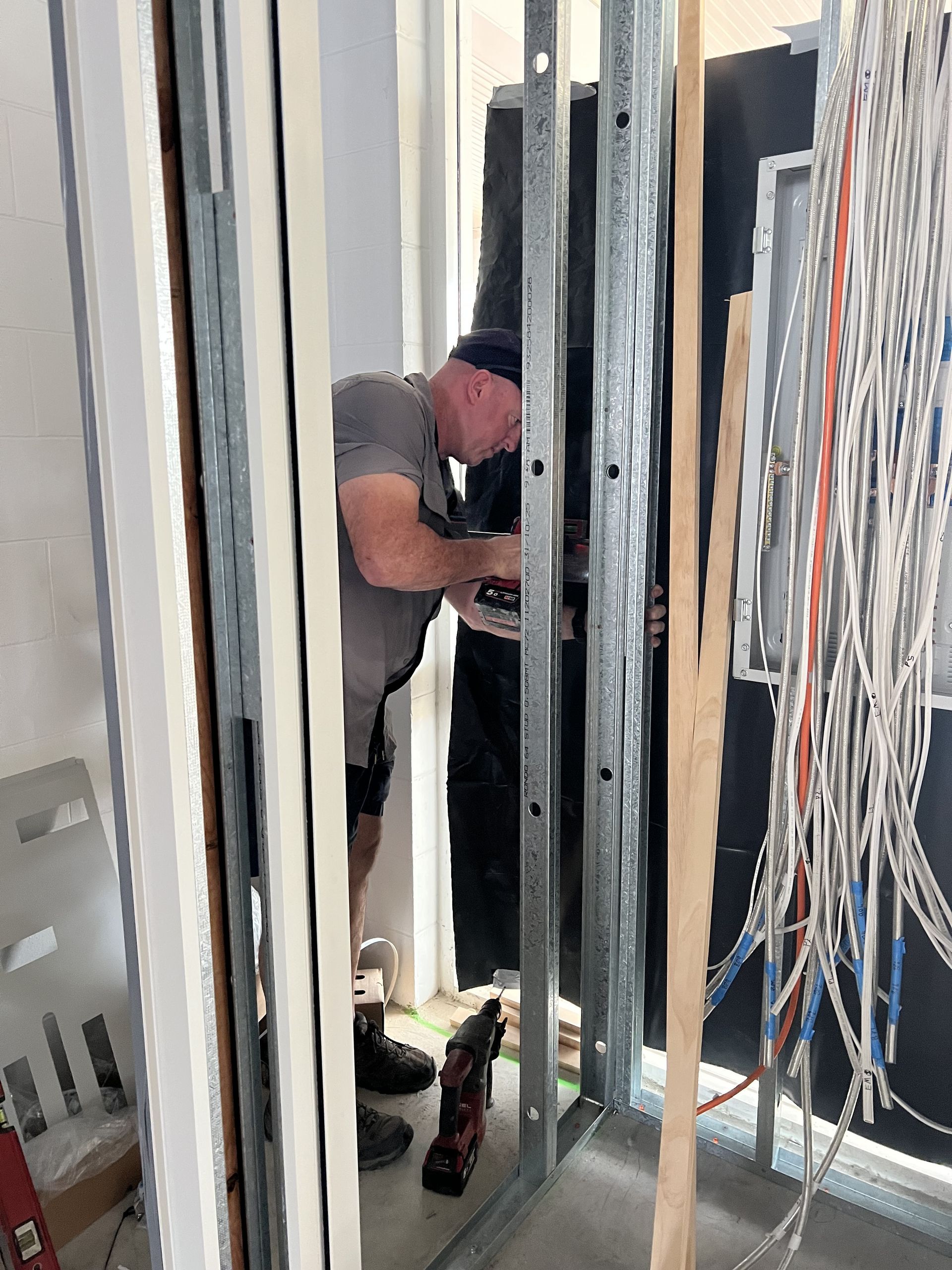 A Worker in a Grey Shirt Uses a Power Drill on Metal Wall — Dunnrite Plumbing Services in Cannonvale, QLD