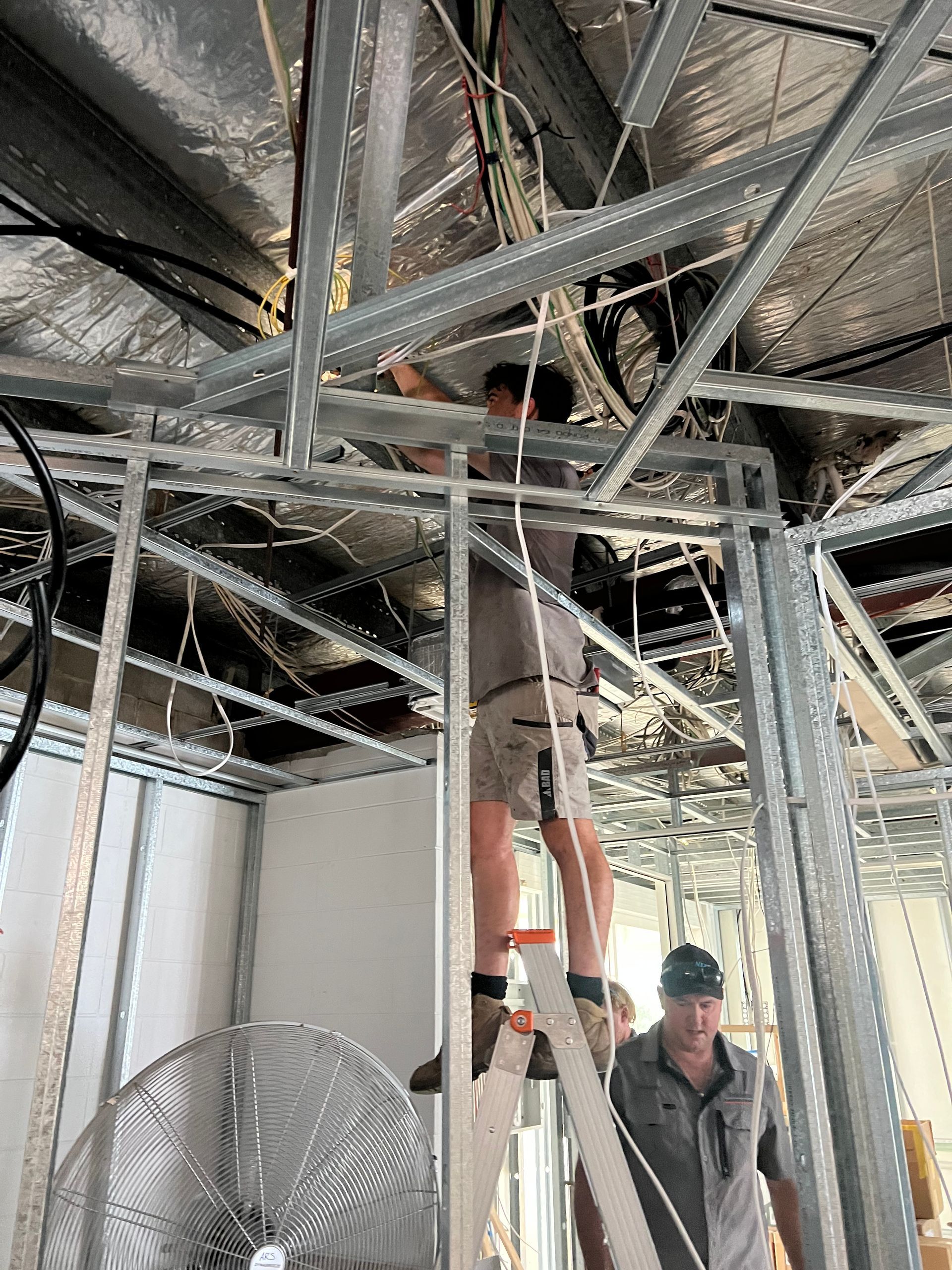 Two Workers Install Wiring in the Metal Ceiling Frame — Dunnrite Plumbing Services in Cannonvale, QLD