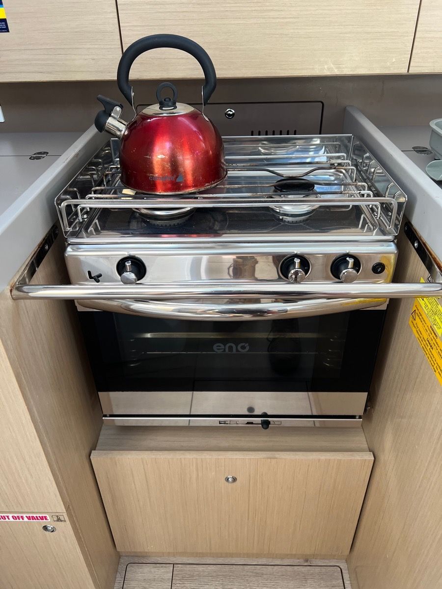 A Stainless Steel Marine Gas Stove With an Oven and a Bright Red Tea Kettle — Dunnrite Plumbing Services in Cannonvale, QLD