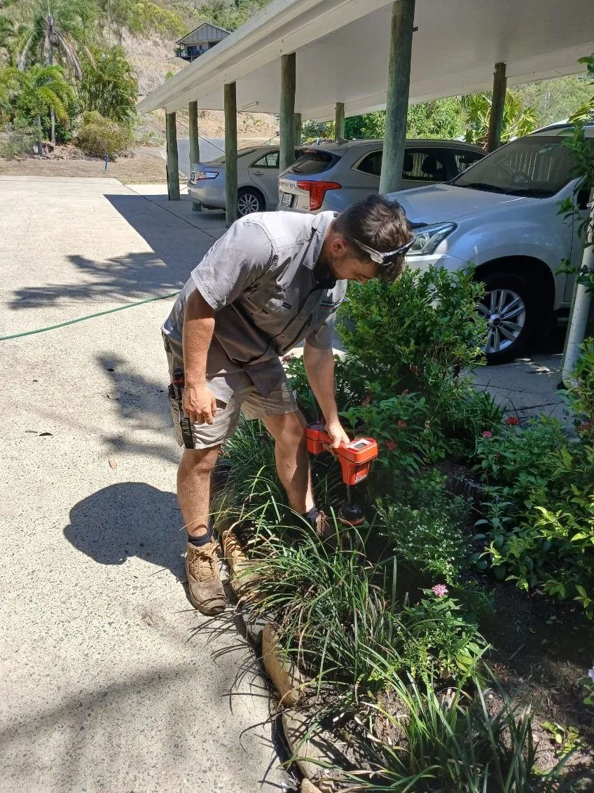 A Person Wearing a Grey Shirt and Shorts Uses an Orange Hand Tool — Dunnrite Plumbing Services in Cannonvale, QLD