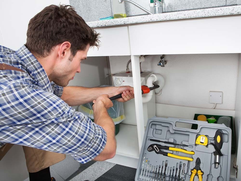A Person in a Plaid Shirt Uses a Wrench to Repair Plumbing Pipes — Dunnrite Plumbing Services in Cannonvale, QLD
