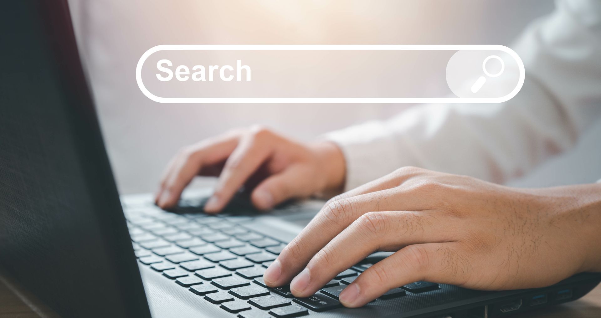 A person is typing on a laptop computer with a search bar on the screen.