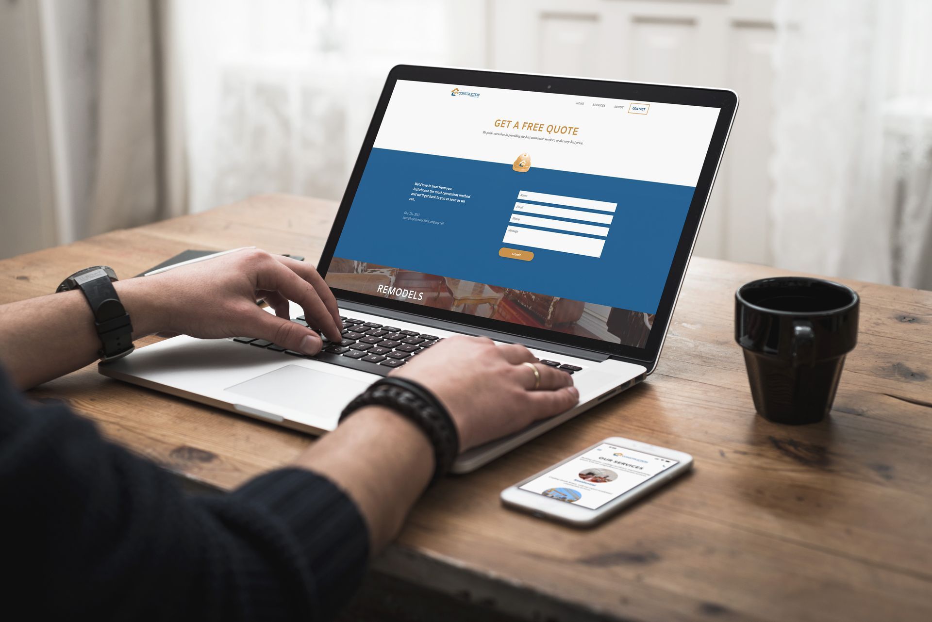 A person is using a laptop on a wooden table open to the My Construction Company website