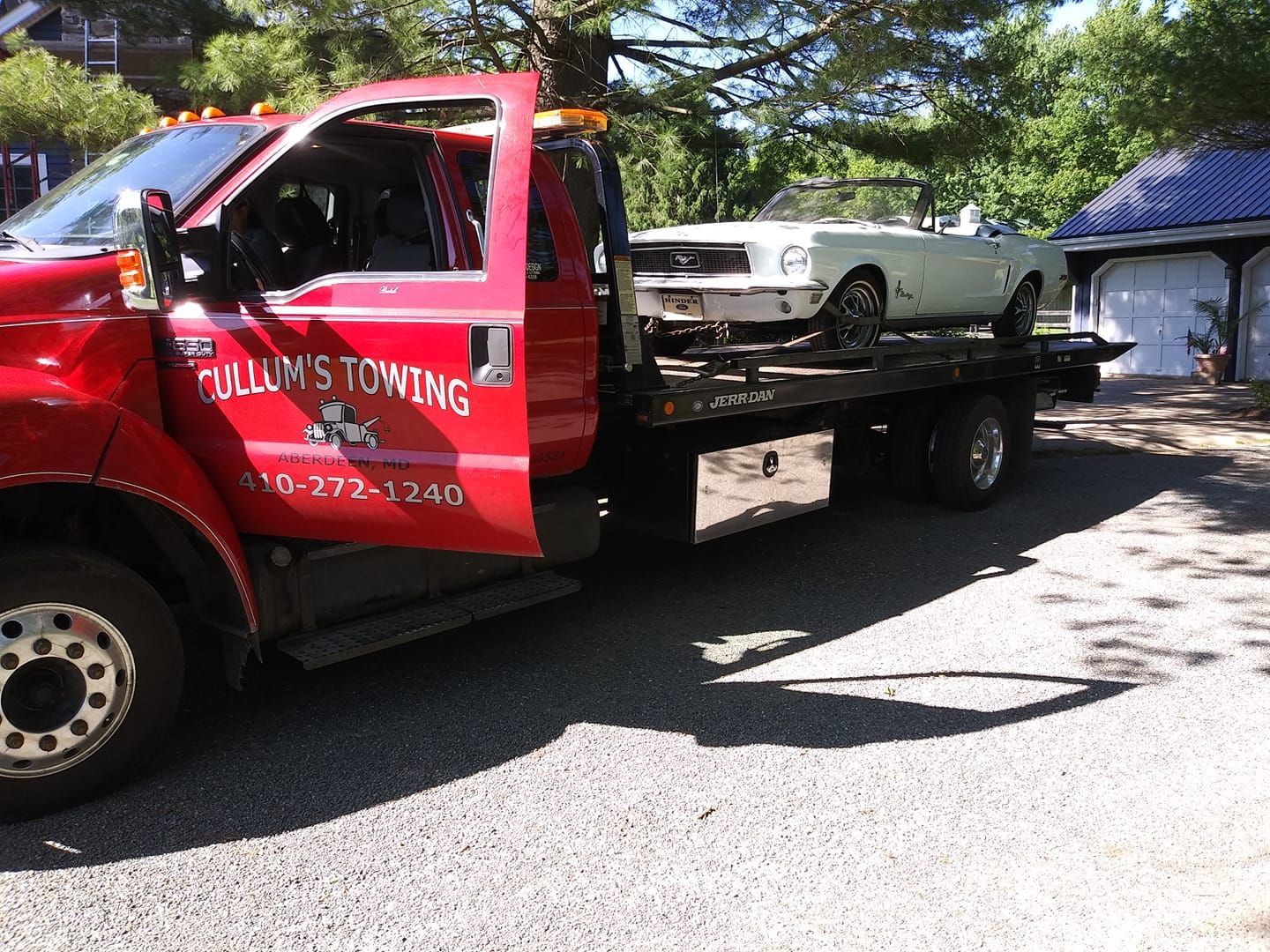 Red tow truck carrying a white car on a flatbed in a driveway, with a garage in the background Red tow truck carrying a white car on a flatbed in a driveway, with a garage in the background