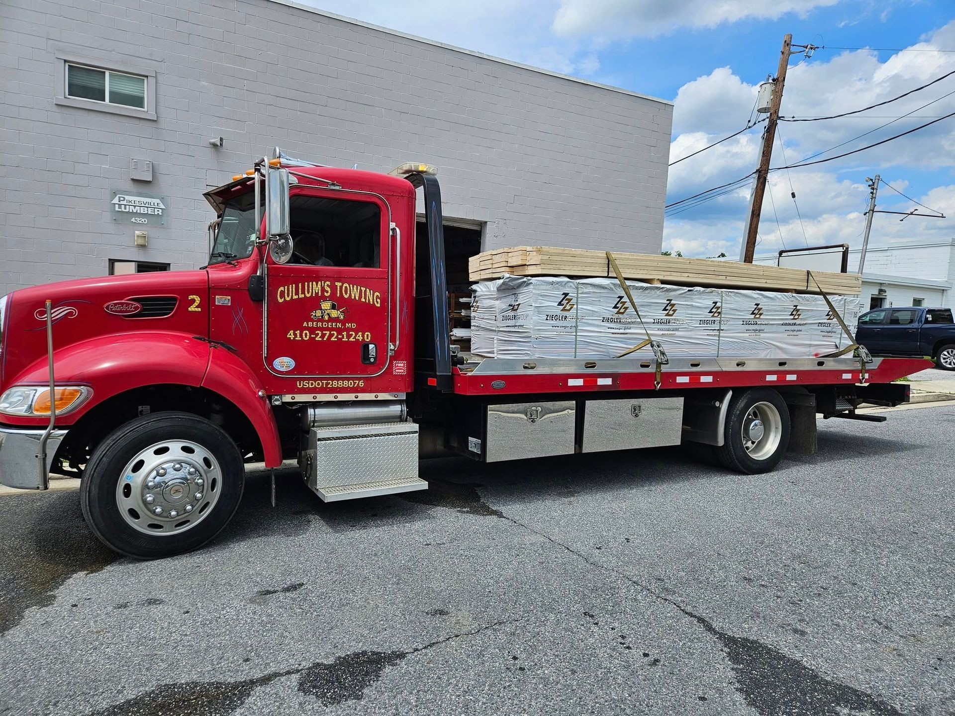 Red flatbed truck loaded with white-wrapped materials parked beside a gray building.