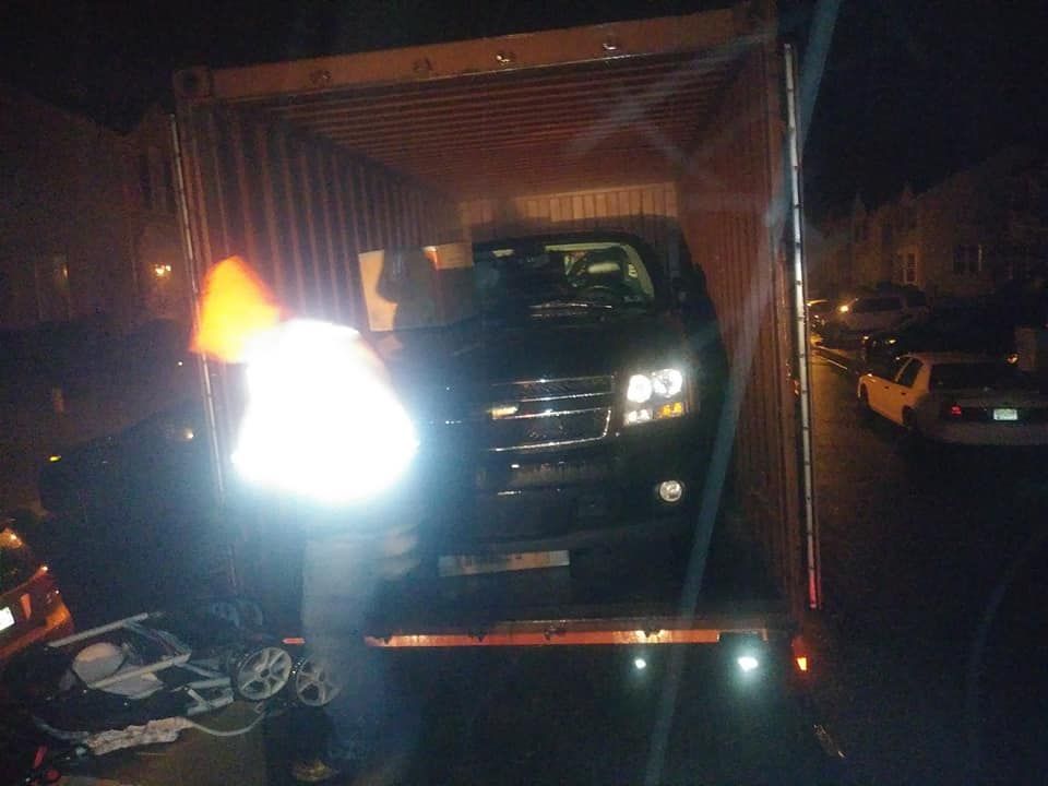 Black SUV inside a lit cargo truck container at night, with another car nearby.