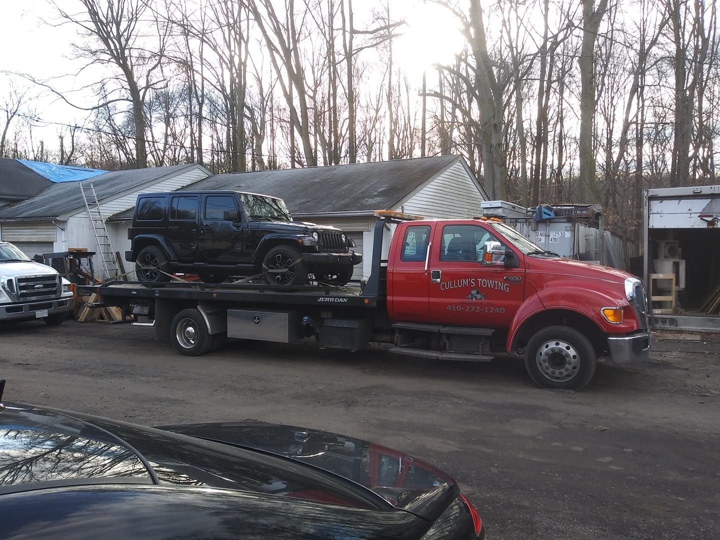Red tow truck carrying a black SUV in a lot beside a low building and bare trees Red tow truck carrying a black SUV in a lot beside a low building and bare trees