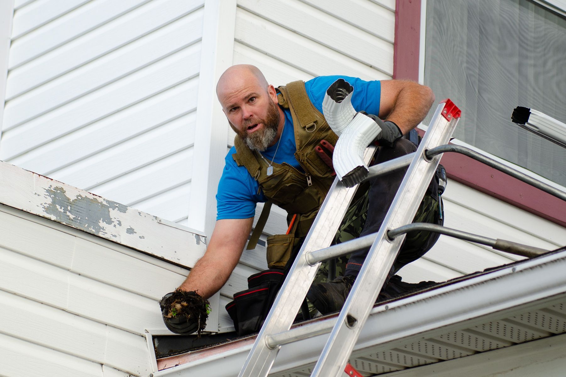 Un homme se tient debout sur une échelle sur le côté d'une maison.