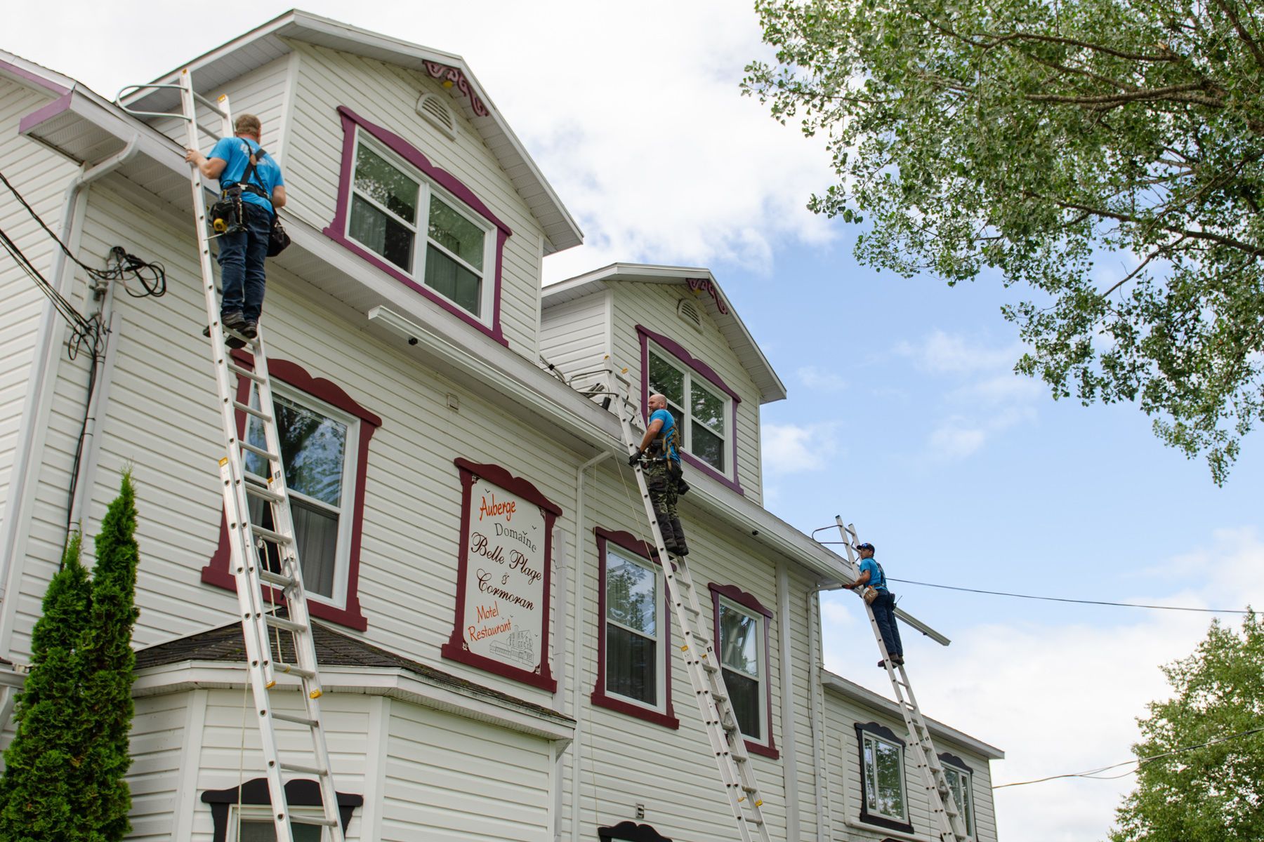Trois hommes peignent le côté d'une grande maison blanche.