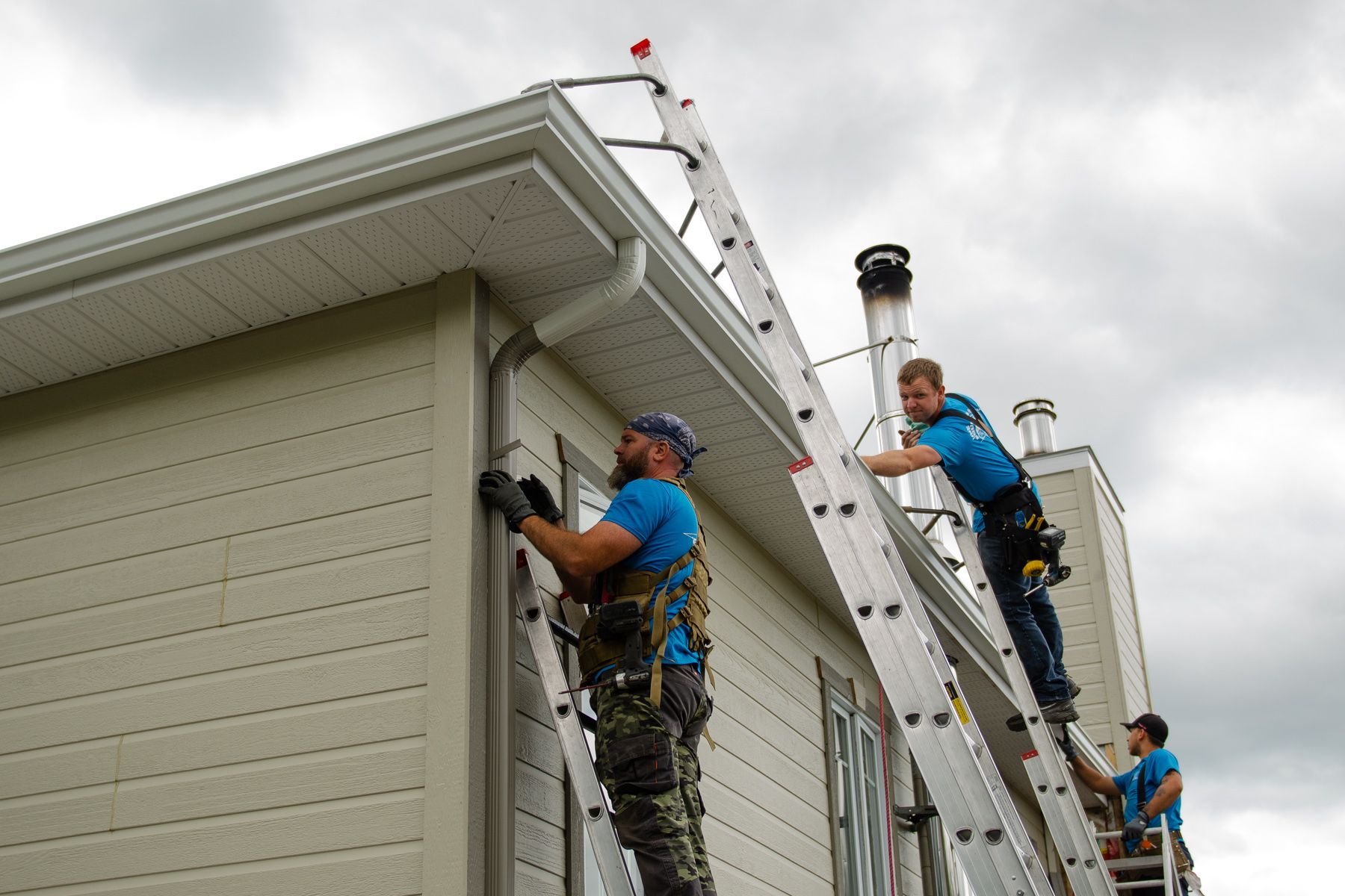 Trois hommes travaillent sur le côté d'une maison avec des échelles.