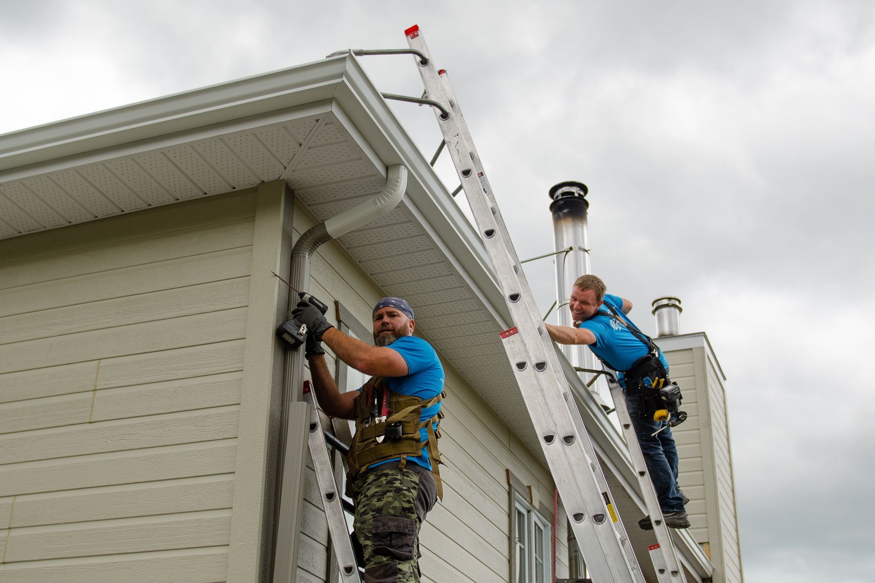 Deux hommes travaillent sur le côté d'une maison avec des échelles.