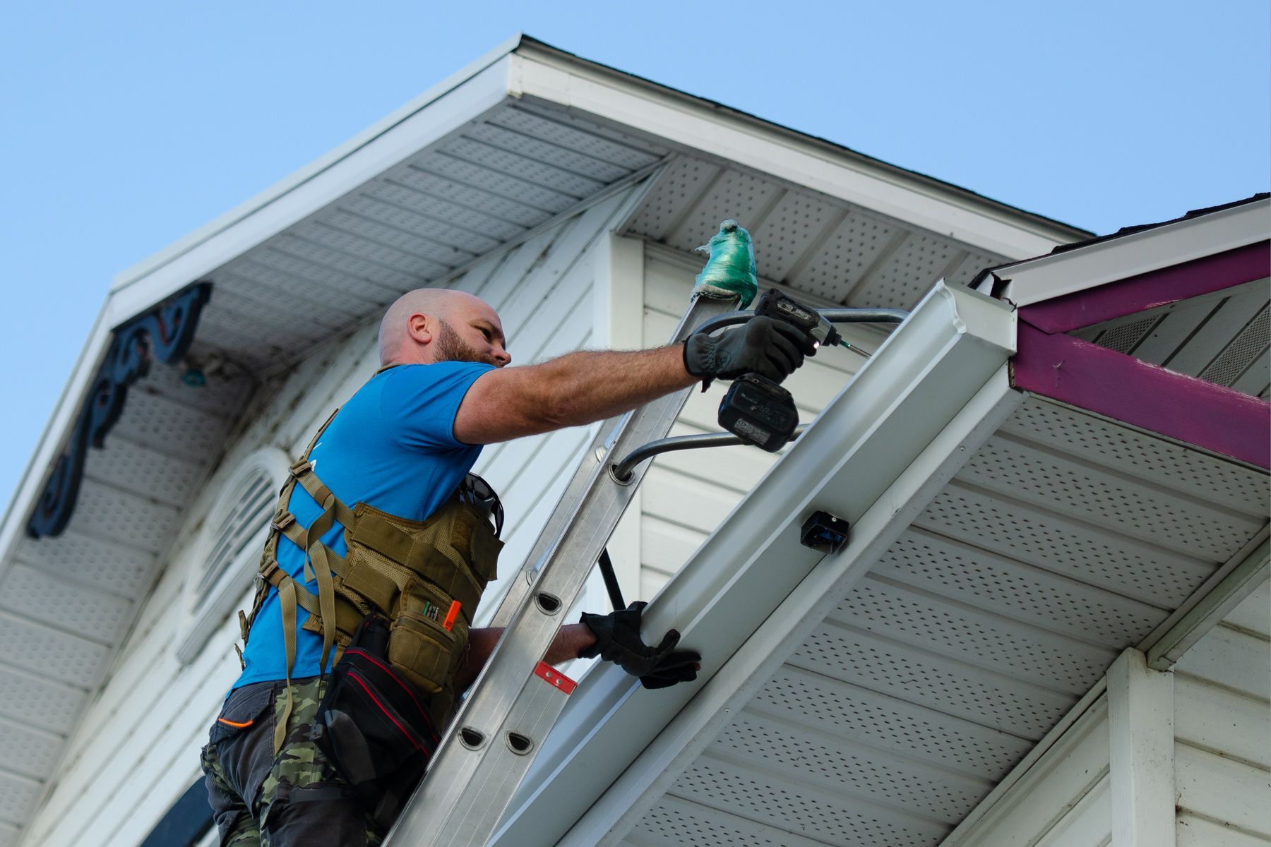 Un homme travaille sur le toit d'une maison avec une perceuse.