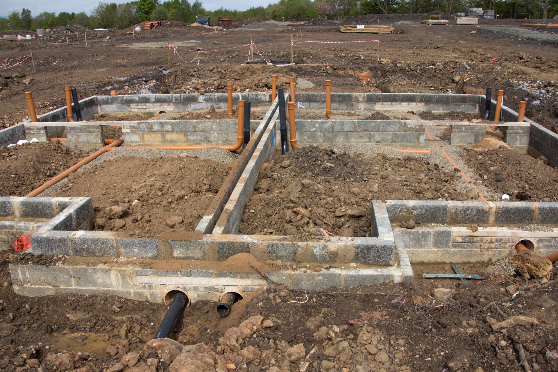 Foundation footings and concrete blocks at a construction site, with dirt trenches and orange markers.