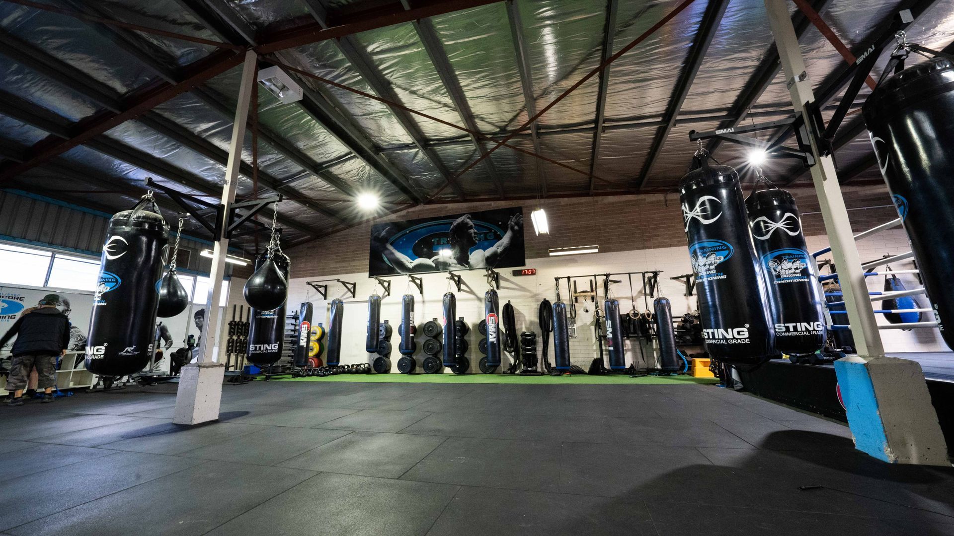 A group of people are standing in a gym with boxing bags hanging from the ceiling.