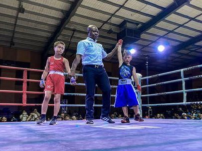 Two young boys are boxing in a ring with a referee.