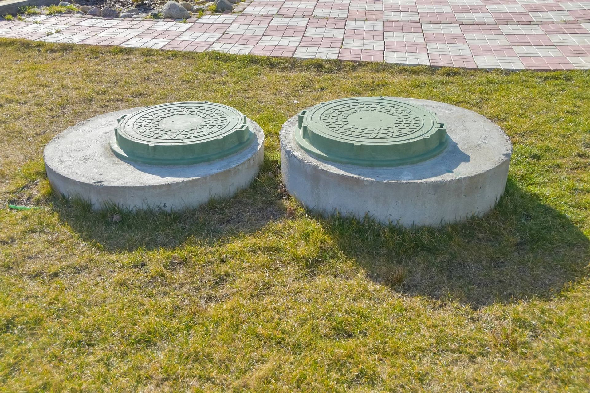 Two round concrete utility covers on grass beside a brick walkway